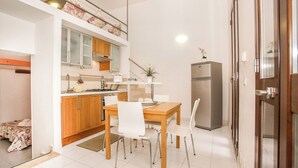 A compact kitchen with wooden cabinets, a stainless steel refrigerator, and a dining area with white chairs. - VERY NICE RENOVATED APARTMENT JUST 20 METERS FROM THE BEACH! (Donnalucata)
