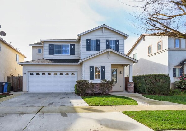 A two-story house with a garage, a small front yard, and a tree.