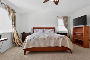 A bedroom with a wooden bed, a television on a stand, a desk, and a wardrobe.