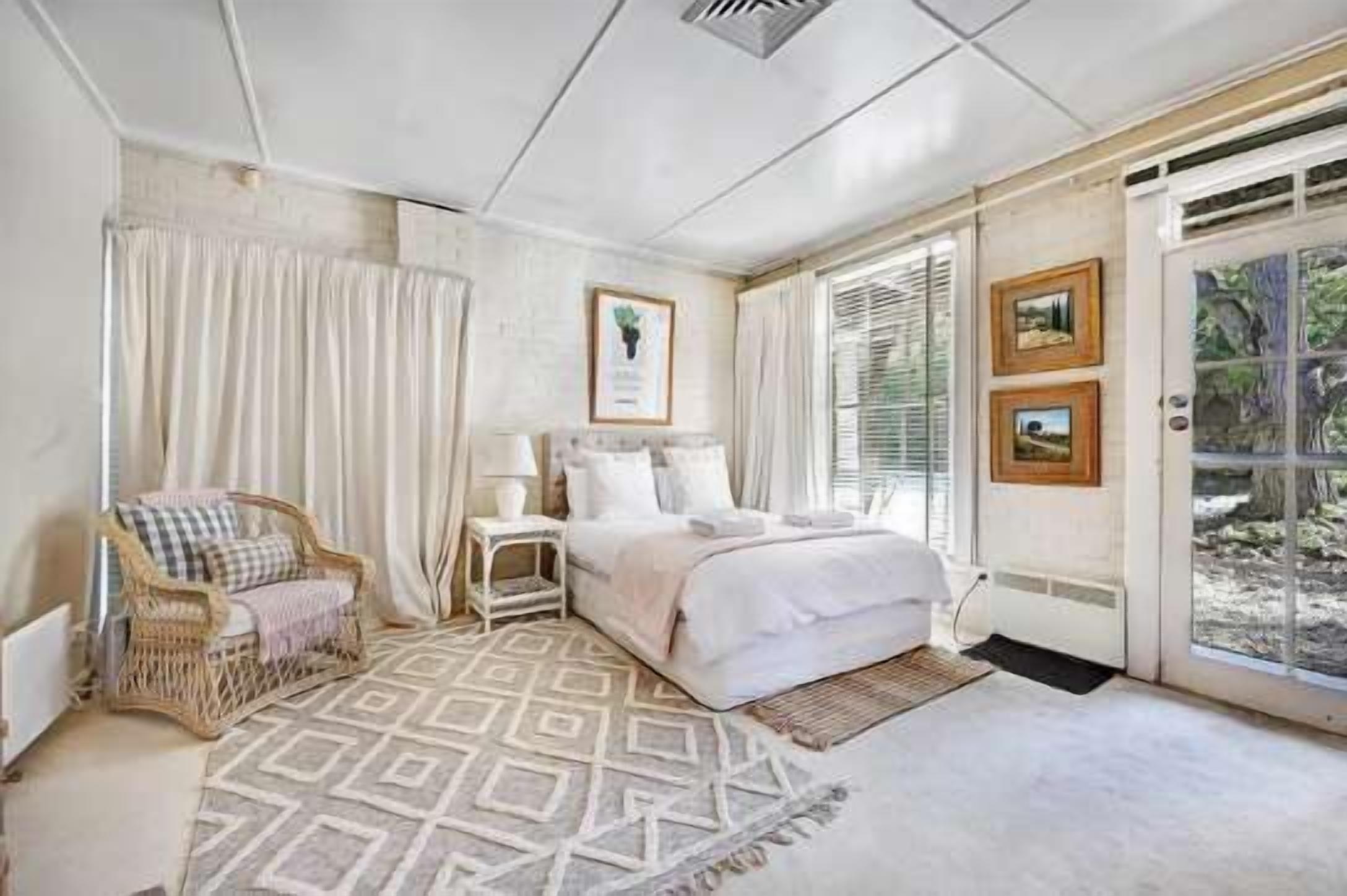 Een slaapkamer met een bed, een stoel, een nachtkastje en een raam met gordijnen.