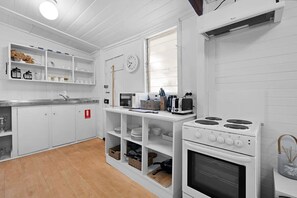 A white kitchen with a stove, microwave, and shelves with dishes and utensils. - Settlers Cottage - Mayfield Vineyard in Orange (Emu Swamp)