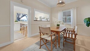 A dining area with a wooden table and chairs, a woven ceiling light fixture, and a view of the kitchen through an open door.