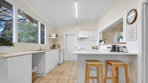 A modern kitchen with white cabinetry, a central island with stools, a large window, and a clock on the wall.