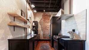 A kitchen with a brick wall, black cabinetry, a wooden countertop, and a rug.