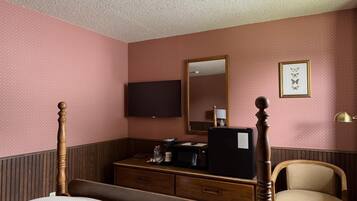 Una habitación de hotel con cama, cómoda, televisor, espejo y silla.