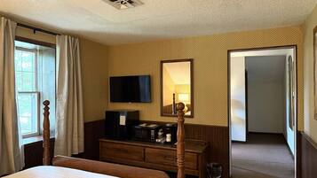 Una habitación de hotel con cama, cómoda, televisor, espejo y puerta que da a otra habitación.