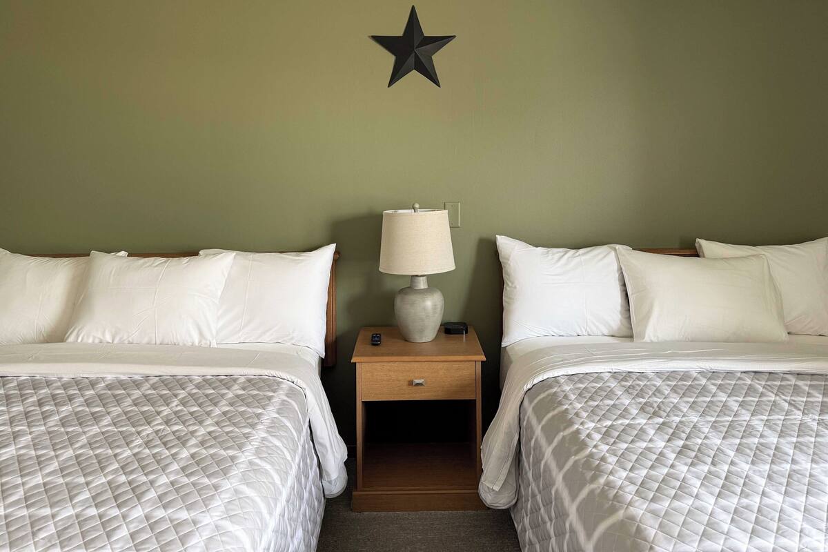A hotel room with two beds, a nightstand with a lamp, and a wall-mounted star decoration.