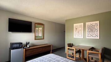 Een hotelkamer met een bed, een bureau, een stoel, een televisie, een kleine koelkast en kunst aan de muren.
