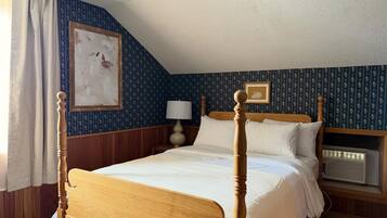 Habitación de hotel con una cama con dosel de madera, una mesita de noche con lámpara, un cuadro enmarcado en la pared y una ventana con cortinas.