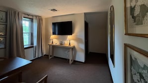 A room with a flat-screen TV, two lamps, a desk, and a chair. - The Trail Inn - Amana IA (Amana)