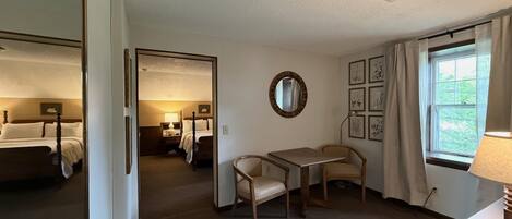 A hotel room with a bed, a desk, a chair, a mirror, a window with curtains, and framed pictures on the wall.