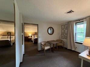 Habitación de hotel con cama, escritorio, silla, espejo, ventana con cortinas y cuadros en la pared.