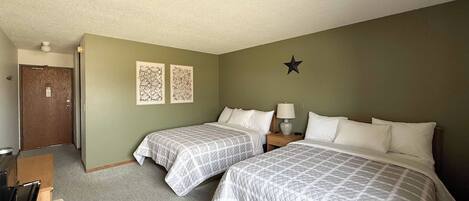 A hotel room with two beds, a desk, a chair, a lamp, and two wall art pieces.