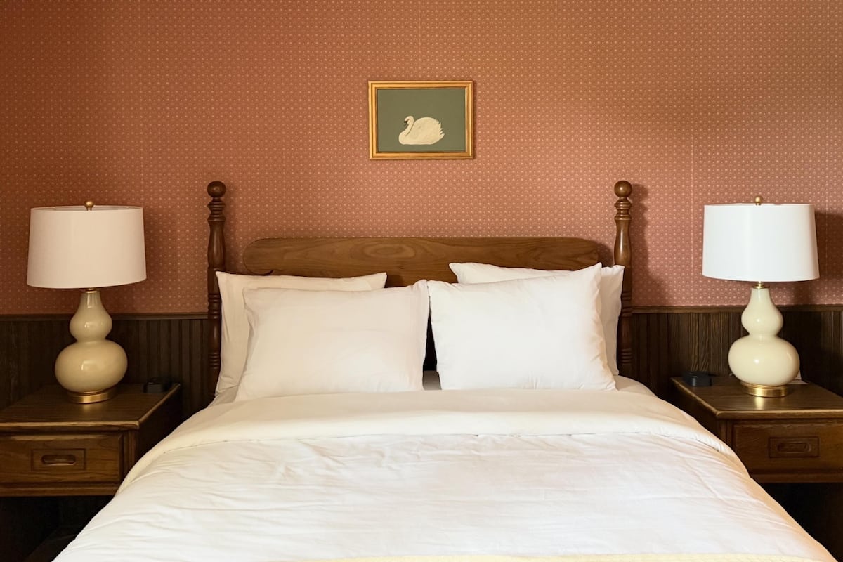 A neatly made bed with white linens, two bedside tables with lamps, and a framed picture on the wall.