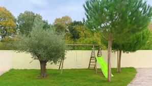 Ein Garten mit Schaukel, einem kleinen Baum und einer Rasenfläche.
