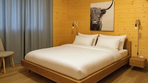 Ein modernes Schlafzimmer mit einem Holzbettgestell, weißer Bettwäsche und einer einzelnen Wandleuchte.