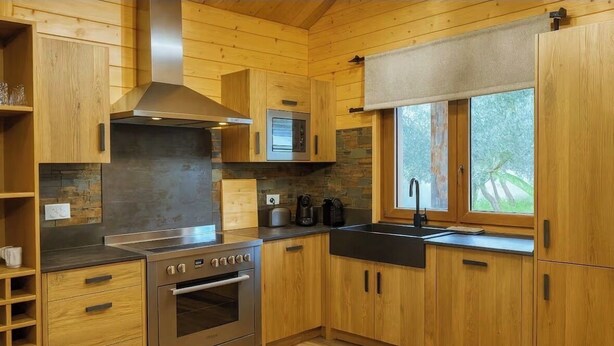 Eine moderne Küche mit Holzschränken, einem Edelstahlbackofen, einer Mikrowelle und einem großen Fenster, das für natürliches Licht sorgt.