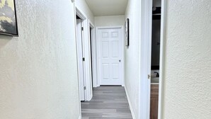 A hallway with white walls, a gray floor, and a white door at the end. - Urban Oasis (Killeen)