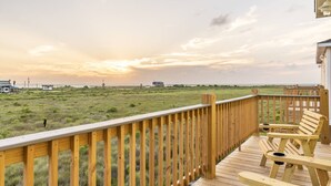 Une terrasse en bois avec une rambarde donnant sur une pelouse, d’où l’on peut admirer le coucher du soleil.