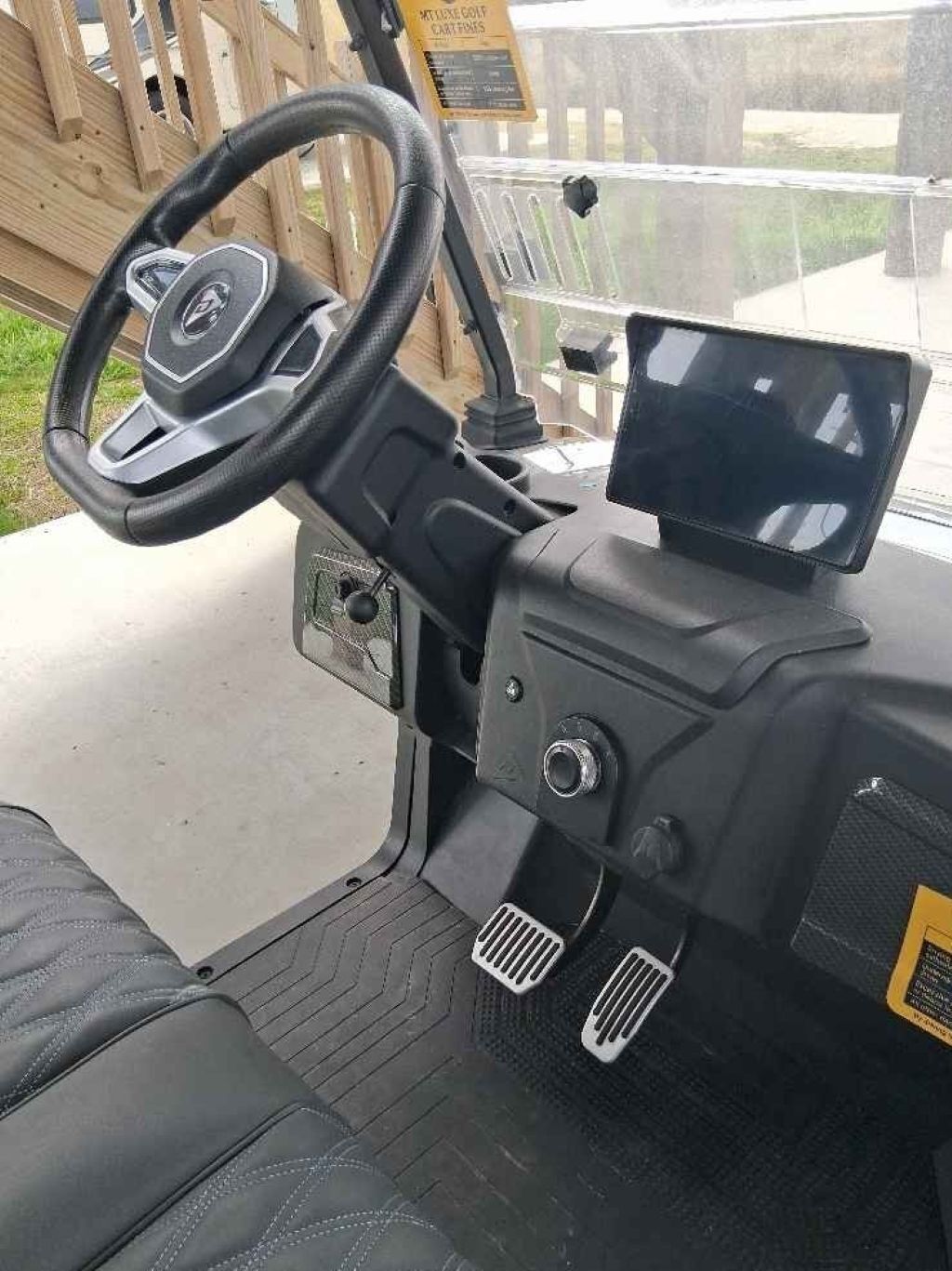 Interior de un carrito de golf, con volante, panel de control y pedales.