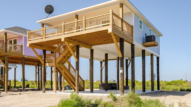 Une maison située en bord de mer, dotée d’une terrasse en bois et d’un balcon.