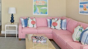 A pink sofa with floral and plaid cushions, a small white side table with a lamp, and a magazine on a wooden coffee table.
