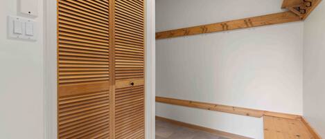 A room with a wooden closet, a wooden bench, and a white wall with a light switch.