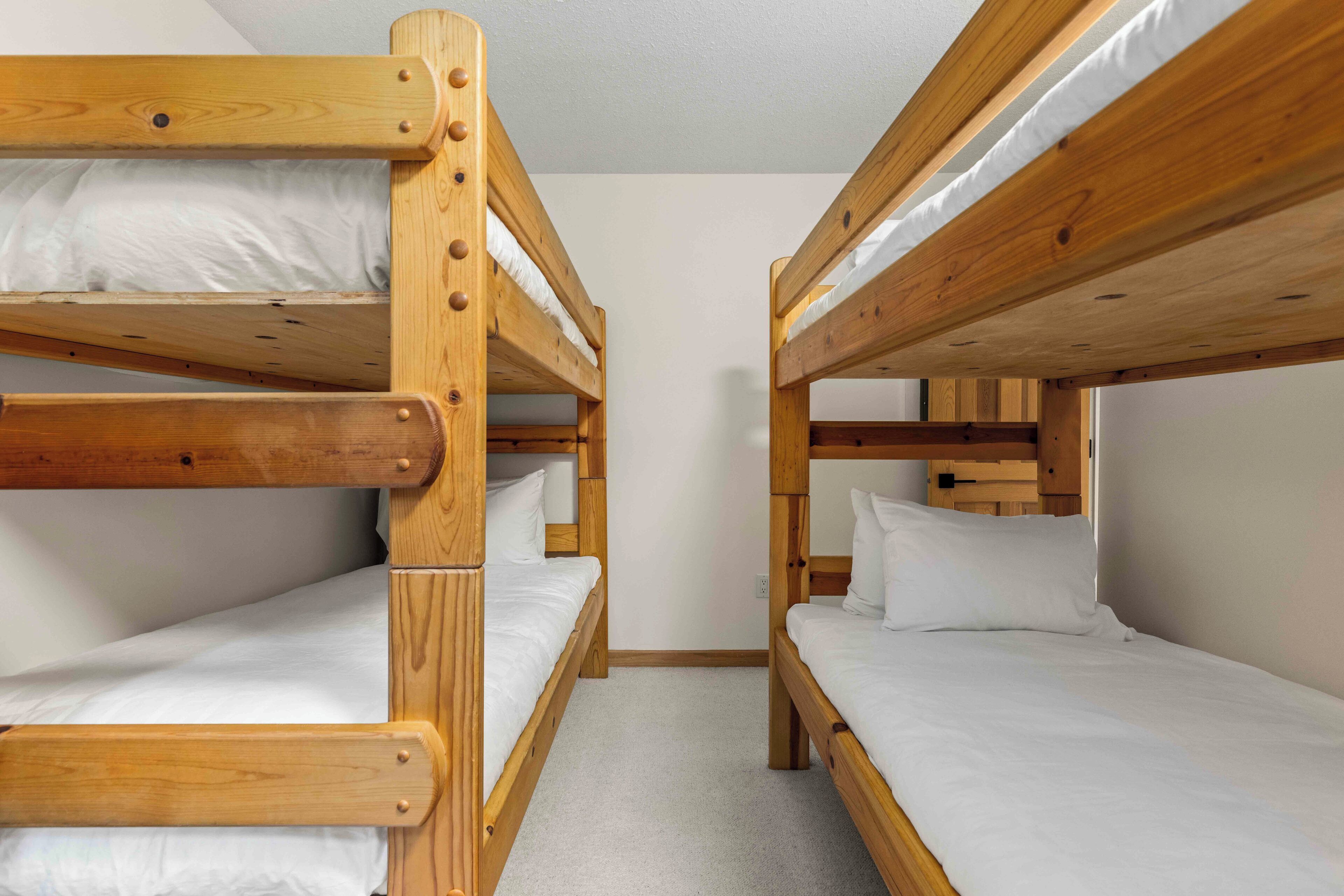 A room with two wooden bunk beds, each with white bedding.
