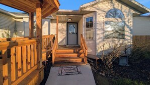 A wooden deck leading to a house with a front door and a welcome mat.