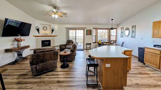 A spacious living room with a fireplace, a ceiling fan, and a large TV.