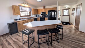 A modern kitchen with wooden cabinets, a black refrigerator, a large island with stools, and a ceiling light.