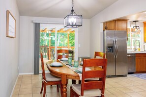 Un comedor con una mesa y sillas de madera, una araña y vistas al exterior a través de una puerta corrediza.