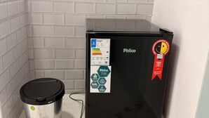A compact black Philco refrigerator with energy efficiency stickers, a recycling bin, and a white tiled wall.