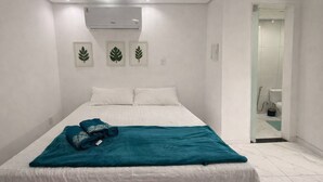 Ein Schlafzimmer mit Bett, weißen Wänden, einer Deckenklimaanlage und gerahmten Blattform-Kunstwerken.