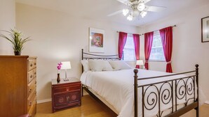 Ein Schlafzimmer mit einem Bett, einem Nachttisch, einer Kommode, einem Deckenventilator und einem Fenster mit Vorhängen.