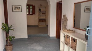 Ein Flur mit einem gewebten Teppich, einer Pendelleuchte, einem Topfpflanzen, einem Holzschrank mit Körben und einem Spiegel an der Wand.