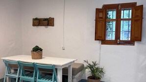 Ein Zimmer mit weißem Tisch, blaugrünen Stühlen, einem Fenster mit Holzjalousien und einer Topfpflanze.