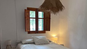 Ein Schlafzimmer mit einem Bett, einem Fenster mit Holzjalousien, einer Pendelleuchte und einem Nachttisch mit Lampe.