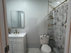 Ein Badezimmer mit weißem Waschbecken, einem Spiegel, einer Toilette und einer Duschvorhang mit Muster.
