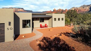 A modern building with a number '50' on the side, a covered patio area with red chairs, and a view of red rock formations in the background. - Red Sky on Caballo Dr. - Great Views & Central (Sedona)