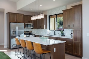 A modern kitchen with wooden cabinets, stainless steel appliances, and a central island with bar stools. - Red Sky on Caballo Dr. - Great Views & Central (Sedona)