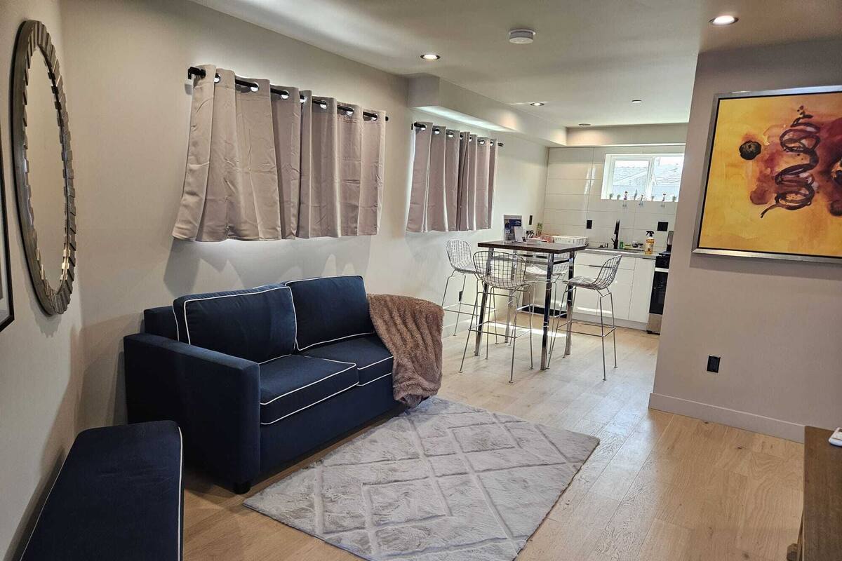 Una sala moderna con un sofá azul oscuro, un tapete estampado y un comedor con sillas de metal y una mesa.