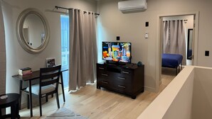 Een moderne slaapkamer met een televisie, een bureau met boeken, een stoel, een bed en een badkamer met douchegordijn.