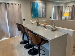 Een moderne keuken met een centraal eiland, barkrukken en een groot schilderij aan de muur.