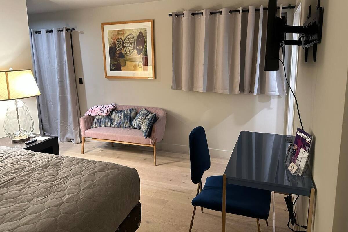 Habitación de hotel con cama, sofá, escritorio, silla, televisor y un cuadro en la pared.