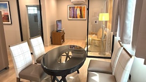 Een moderne hotelkamer met een glazen tafel, twee comfortabele stoelen, een bank, een klein houten kastje en een schilderij aan de muur.