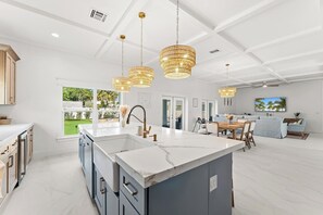 A spacious kitchen with a large island, pendant lights, and a view to the outdoors. - Diamond Sands| Epic Mini Golf| Guest House (Jensen Beach)