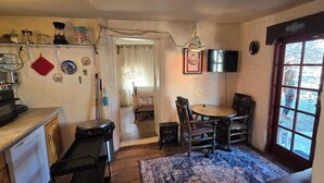 A compact kitchen with a dining area, a TV mounted on the wall, and a large window with a view. - Cozy 2-bedroom cabin on a working mini farm in San Fidel with AC on old route 66 (San Fidel)