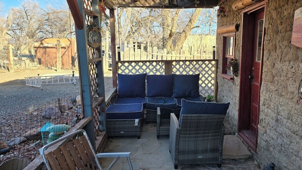 A covered outdoor seating area with wicker furniture and a red door. - Cozy 2-bedroom cabin on a working mini farm in San Fidel with AC on old route 66 (San Fidel)