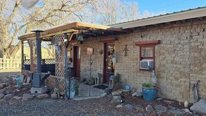 A rustic stone building with a covered porch, a small window, and a potted plant. - Cozy 2-bedroom cabin on a working mini farm in San Fidel with AC on old route 66 (San Fidel)